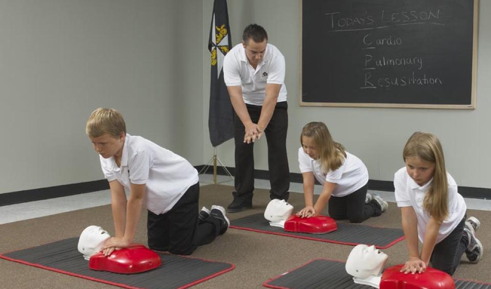 A group of children learning CPR from an SJA first aid instructor.