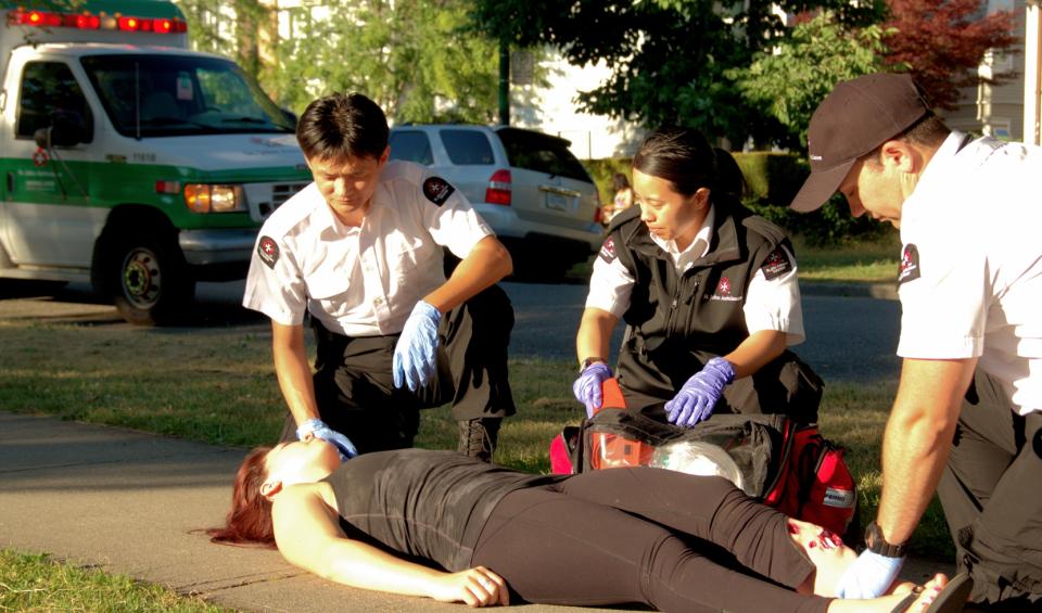 3 SJA Medical First Responders helping a woman who is a patient lying on the ground outside.