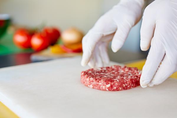 Person handling hamburger meat patty with gloves